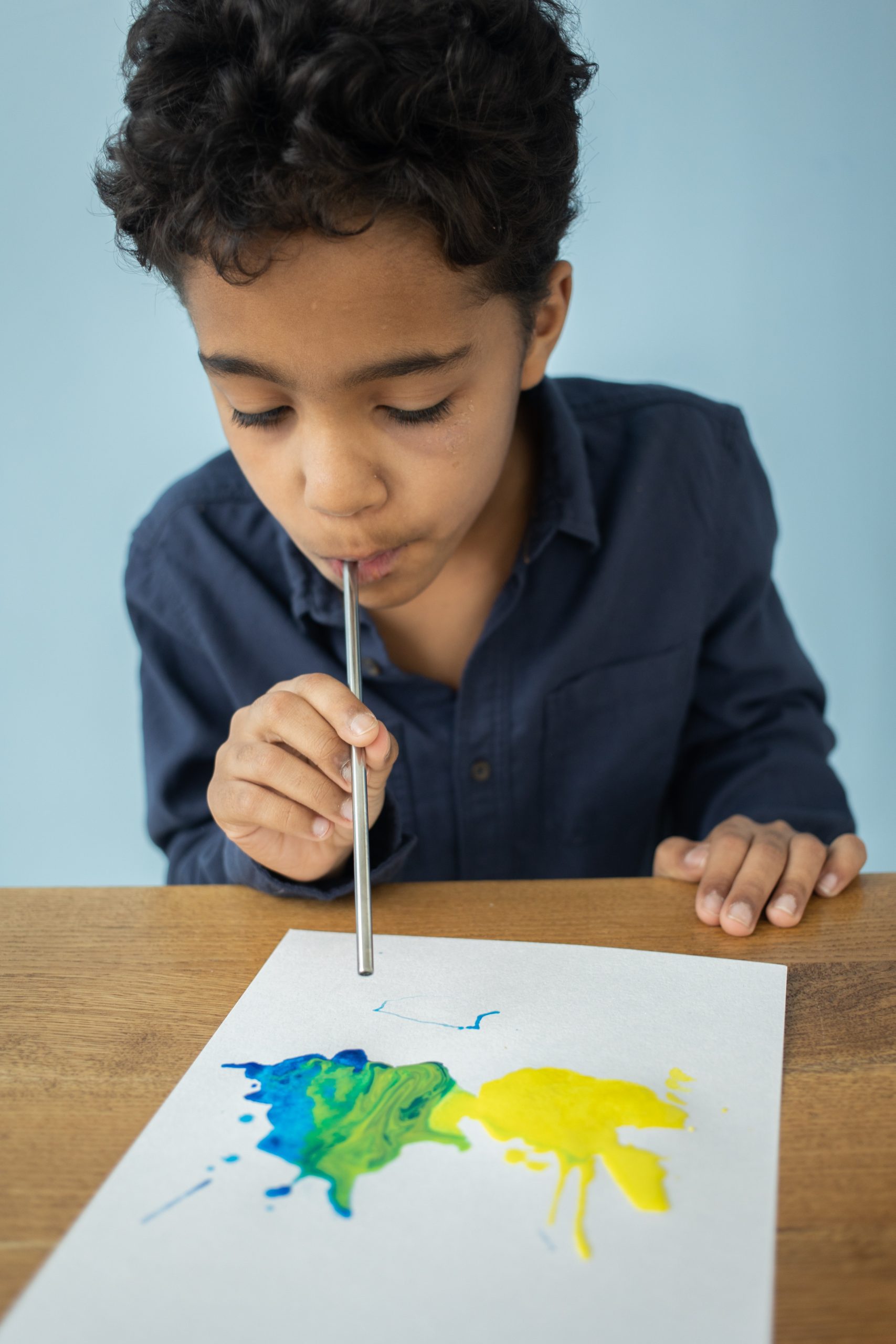 Young boy blowing paint on paper